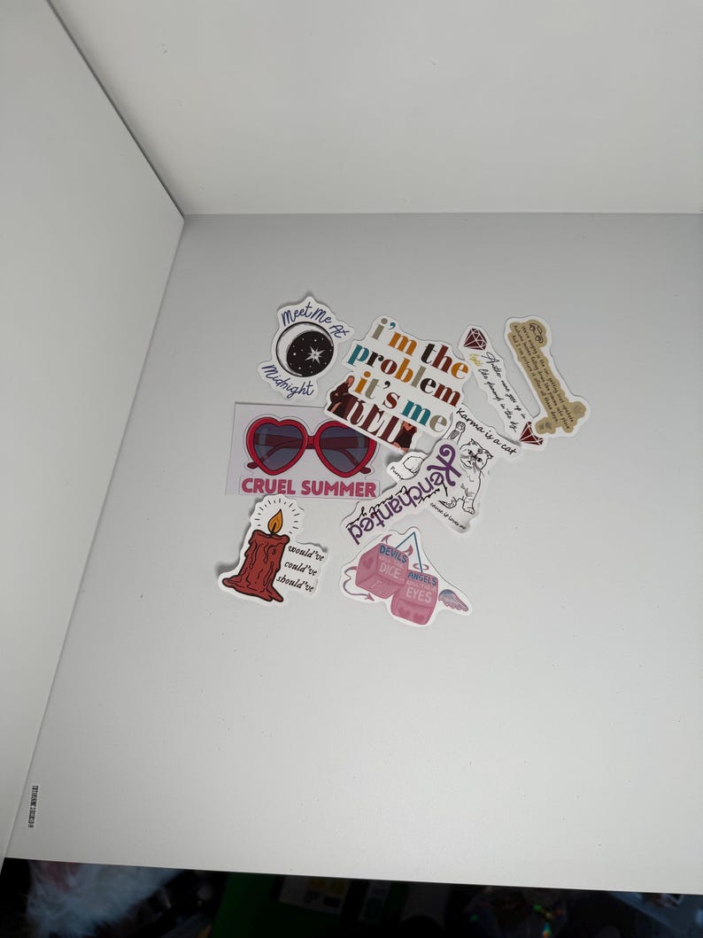 May include: A collection of colorful stickers with various designs and text. Stickers include heart-shaped sunglasses, a burning candle, and phrases like "I'm the problem, it's me" and "Cruel Summer".