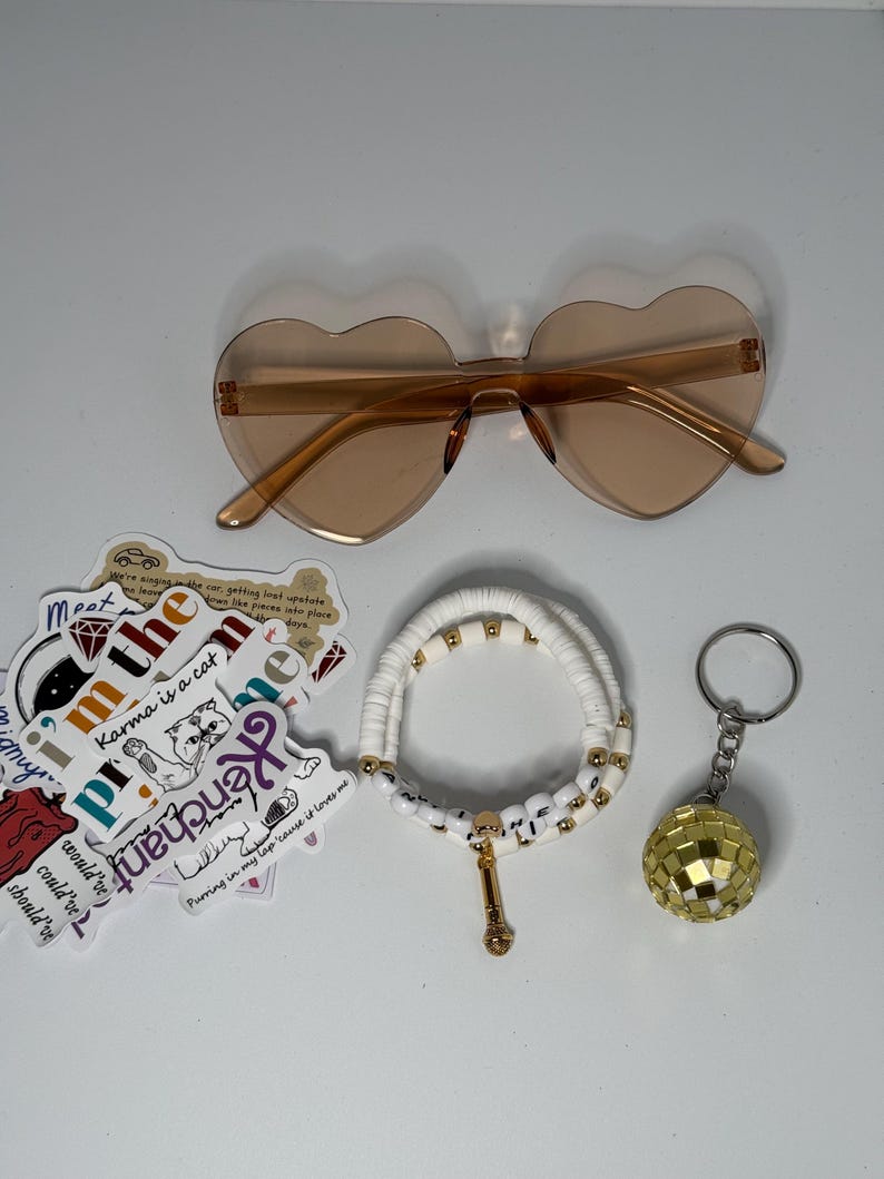 May include: A collection of accessories including heart-shaped sunglasses, a white beaded bracelet with gold accents, a disco ball keychain, and stickers with various phrases and graphics.