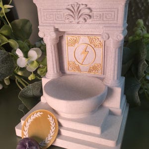 White marble style Greek altar shrine with classical column details and a raised offering bowl, designed as altar decor for ritual or devotional use. The shrine features a central display relief depicting Zeus’s lightning bolt as the focal symbolic element of the piece.