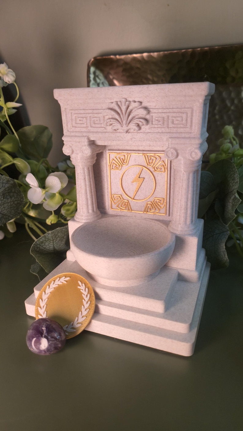 White marble style Greek altar shrine with classical column details and a raised offering bowl, designed as altar decor for ritual or devotional use. The shrine features a central display relief depicting Zeus’s lightning bolt as the focal symbolic element of the piece.