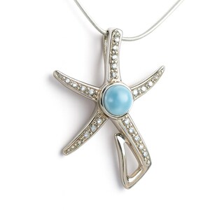 May include: Silver starfish pendant necklace with a light blue gemstone center and small clear stones along the arms. The pendant hangs from a thin silver chain. A jewelry item.