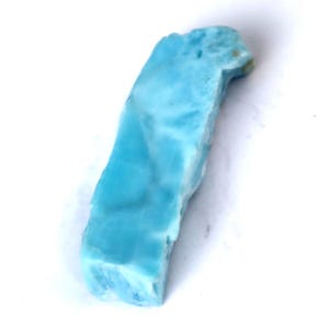 May include: A piece of raw larimar gemstone, showcasing a vibrant blue hue with white marbling. The stone has a natural, irregular shape, and is set against a plain white background. This gemstone is a beautiful example of natural mineral formations.