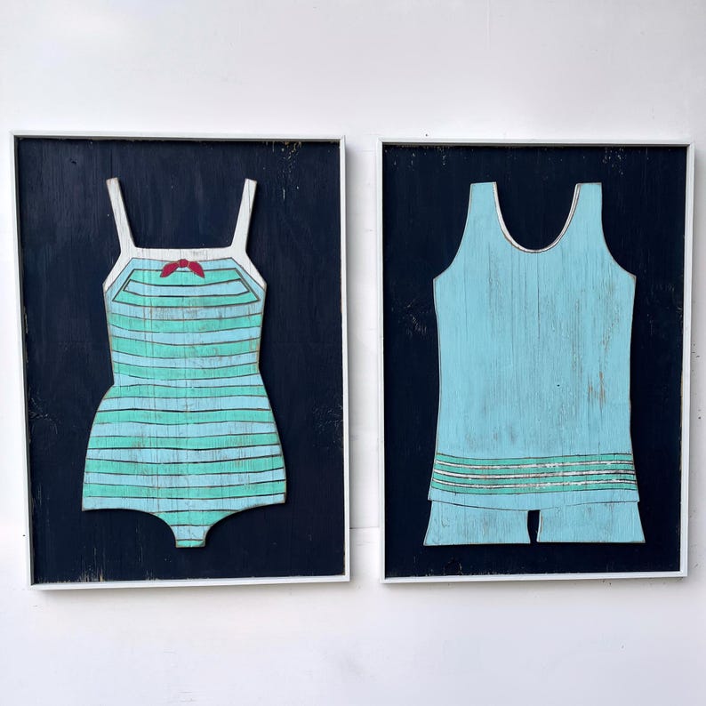 Pu&ograve; includere: Due opere d'arte in legno incorniciate. Una raffigura un costume da bagno a righe turchese e azzurre con un fiocco rosso. L'altra &egrave; un costume da bagno azzurro con pantaloncini. Entrambe sono su sfondo blu scuro.