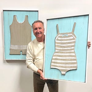 Pu&ograve; includere: Due opere d'arte da parete incorniciate con disegni di costumi da bagno vintage. Uno &egrave; un costume intero marrone chiaro con strisce bianche, l'altro &egrave; un costume a canotta marrone chiaro. Entrambi sono ambientati su uno sfondo azzurro chiaro all'interno di cornici bianche.