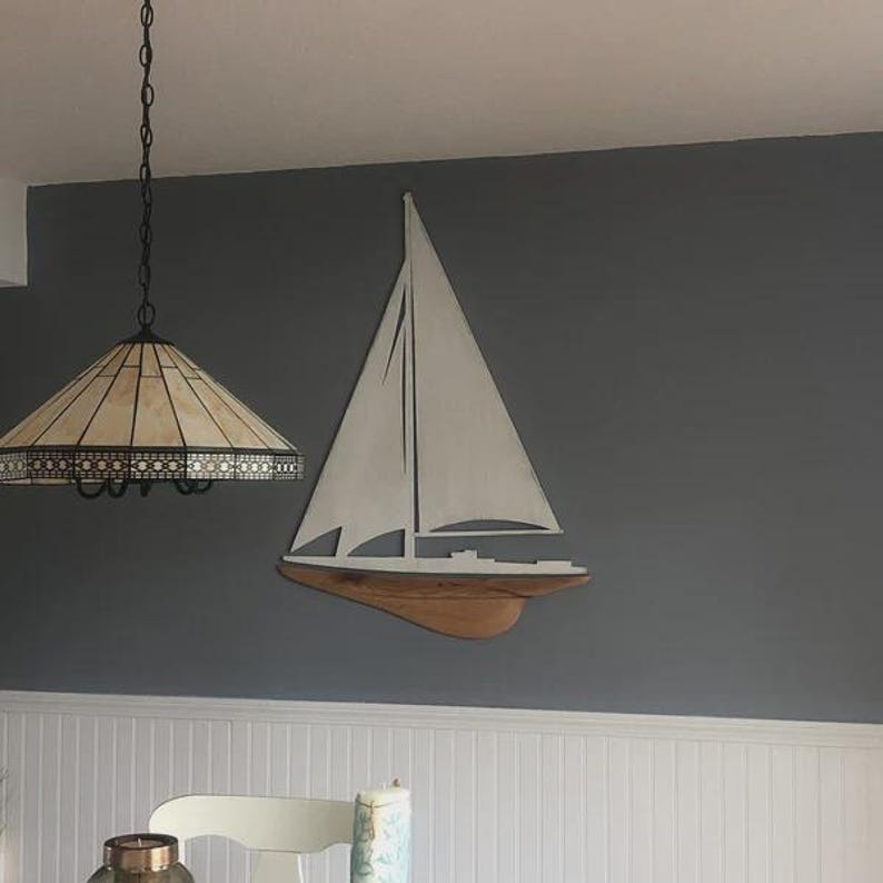 May include: A wooden sailboat wall decoration with white sails and a brown hull is mounted on a gray wall. The sailboat is a nautical-themed piece. A decorative lamp hangs from the ceiling.