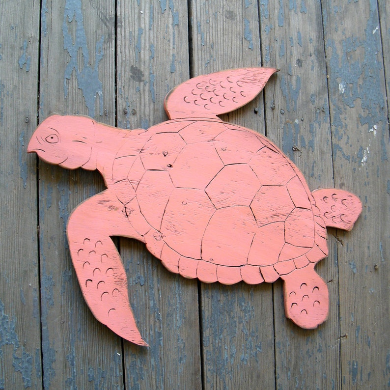 May include: A pink wooden turtle cutout with a detailed shell design. The turtle is mounted on a weathered wooden surface.