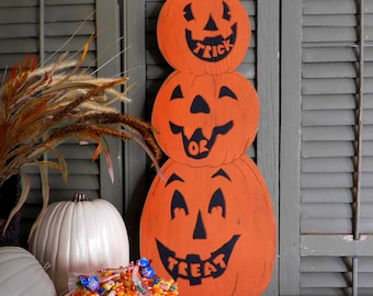 Puede incluir: Decoración de calabaza de madera naranja apilada con las palabras "Trick or Treat" en negro. La decoración de Halloween se muestra con calabazas blancas y un cubo de metal lleno de caramelos.
