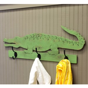 May include: Green wooden alligator wall hook with three black metal hooks. Two towels are hanging on the hooks.