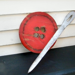 May include: A large red wooden button with four holes, and a long silver needle.