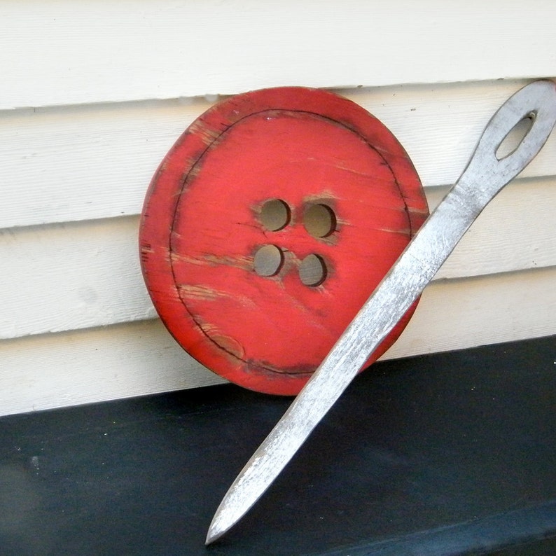 May include: A large red wooden button with four holes, and a long silver needle.