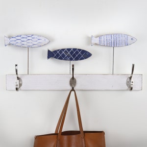 May include: White wooden coat rack with three hooks, each featuring a blue and white painted fish design. A brown leather tote bag hangs from one of the hooks.