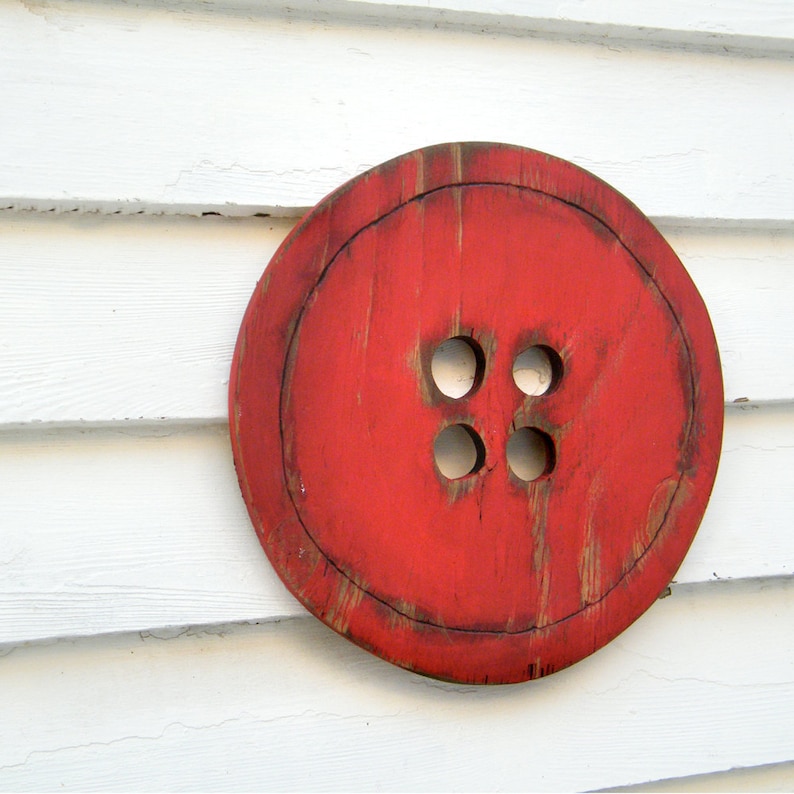 May include: A large, red wooden button with four holes in the center. The button is painted a bright red and has a distressed, rustic look.