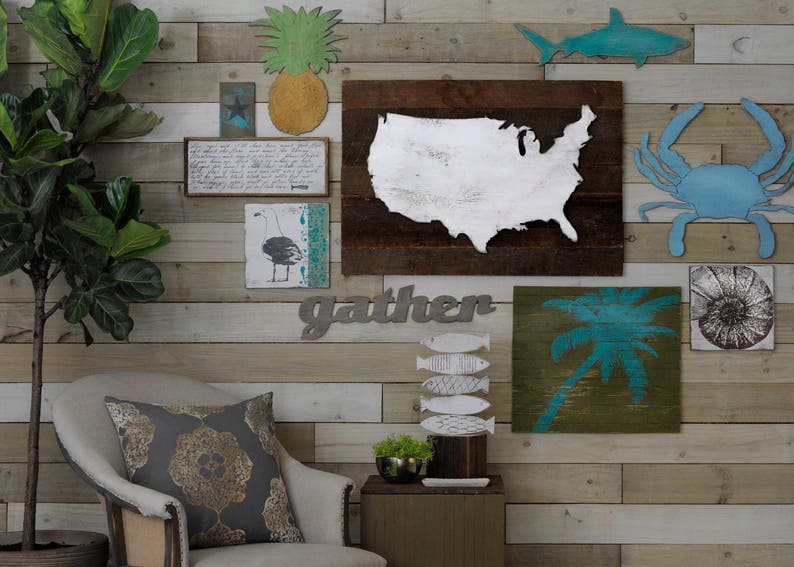 May include: A wall decor set with a nautical theme. The set includes a wooden sign with the word "gather" in metal letters, a wooden sign with a blue silhouette of a palm tree, a wooden sign with a blue silhouette of a crab, a wooden sign with a blue silhouette of a shark, a wooden sign with a white silhouette of the United States, a wooden sign with a blue silhouette of a seagull, and a wooden sign with a blue and white silhouette of a pineapple.