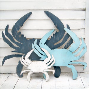 May include: Three wooden crab wall decor pieces in different sizes. The largest crab is dark blue, the medium crab is light blue, and the smallest crab is white.