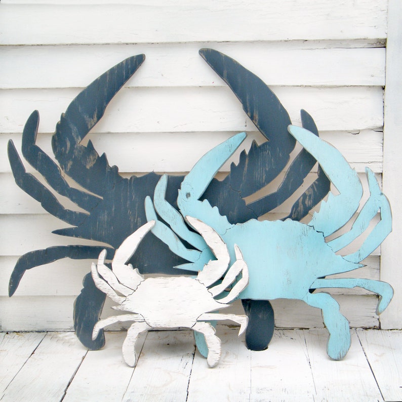 May include: Three wooden crab wall decor pieces in different sizes. The largest crab is dark blue, the medium crab is light blue, and the smallest crab is white.