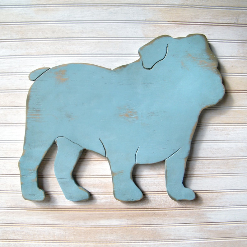 May include: A light blue wooden cutout of a bulldog, painted in a distressed style. The cutout is standing on a white wood background.
