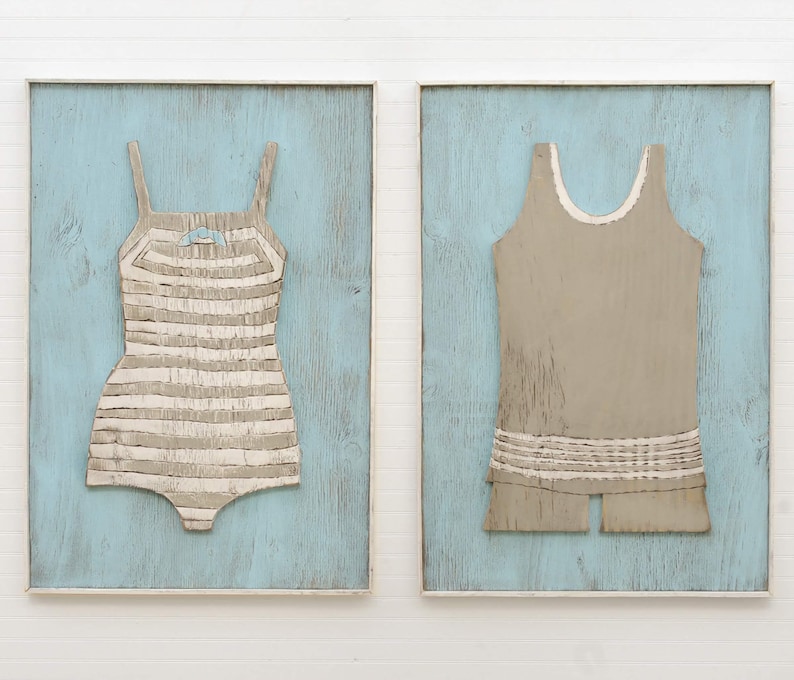 Pu&ograve; includere: Due opere d'arte incorniciate raffiguranti costumi da bagno vintage. Uno &egrave; un costume da bagno a righe beige e bianco con un fiocco. L'altro &egrave; un costume da bagno beige tinta unita con finiture bianche. Entrambi sono su uno sfondo di legno azzurro.