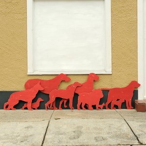 May include: A collection of red wooden dog silhouettes of various sizes, arranged in a row on a wall with a white window behind them.