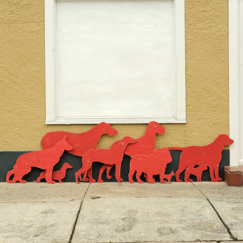 May include: A collection of red wooden dog silhouettes of various sizes, arranged in a row on a wall with a white window behind them.