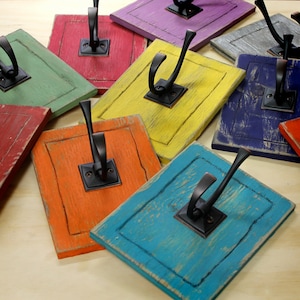 May include: A set of nine colorful wooden hooks with black metal hooks. The hooks are painted in various colors, including blue, green, yellow, orange, and red. The hooks are distressed and have a rustic look.
