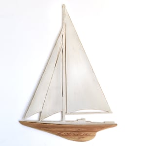 May include: A wooden sailboat wall art piece. The sails are painted white, and the hull is a natural wood grain. The sailboat is a decorative item, perfect for nautical-themed decor. The design is simple and elegant.