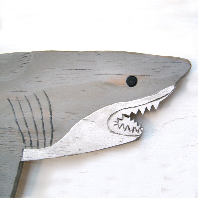 May include: A gray wooden shark with a white painted mouth and black eye. The shark is carved with details like gills and teeth.
