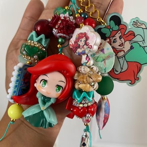 Peut inclure: Un porte-cl&eacute;s color&eacute; avec divers breloques et perles. Les breloques comprennent des images de personnages de dessins anim&eacute;s, des accents en forme de c&oelig;ur et des perles d&eacute;coratives rouges, vertes et dor&eacute;es. Le porte-cl&eacute;s est attach&eacute; &agrave; un fermoir dor&eacute;.