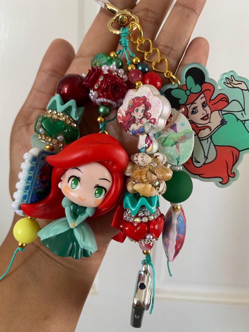 Peut inclure: Un porte-cl&eacute;s color&eacute; avec divers breloques et perles. Les breloques comprennent des images de personnages de dessins anim&eacute;s, des accents en forme de c&oelig;ur et des perles d&eacute;coratives rouges, vertes et dor&eacute;es. Le porte-cl&eacute;s est attach&eacute; &agrave; un fermoir dor&eacute;.