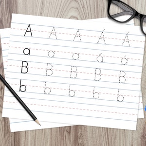 Puede incluir: Un papel blanco con l&iacute;neas y l&iacute;neas punteadas para trazar las letras A y B. Las letras est&aacute;n impresas en tinta negra. Un l&aacute;piz y un vaso de bol&iacute;grafos est&aacute;n sobre una superficie de madera.