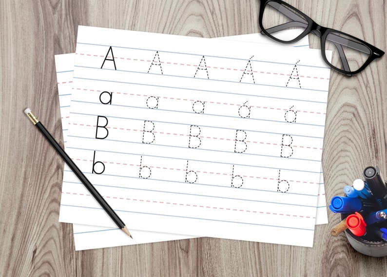 Puede incluir: Un papel blanco con l&iacute;neas y l&iacute;neas punteadas para trazar las letras A y B. Las letras est&aacute;n impresas en tinta negra. Un l&aacute;piz y un vaso de bol&iacute;grafos est&aacute;n sobre una superficie de madera.