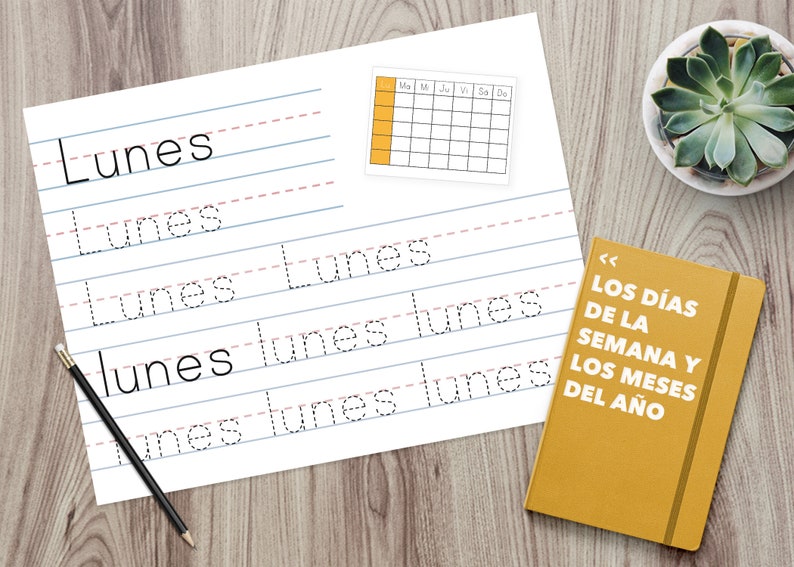 Puede incluir: Una hoja de papel blanca con l&iacute;neas de escritura para practicar la escritura de la palabra espa&ntilde;ola "Lunes" (lunes). El papel est&aacute; sobre una superficie de madera con un calendario amarillo y un libro amarillo con el texto "LOS D&Iacute;AS DE LA SEMANA Y LOS MESES DEL A&Ntilde;O" (Los d&iacute;as de la semana y los meses del a&ntilde;o).