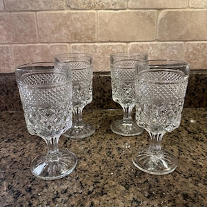 May include: Four clear, vintage-style goblets with diamond-patterned glass. The stemmed glasses have a classic design, perfect for serving beverages. The goblets are displayed on a speckled countertop.