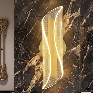 May include: A vertical wall sconce featuring a cylindrical light source encased in a curved, translucent acrylic panel with a fine dot pattern. The fixture emits a warm, glowing light and is mounted on a circular gold-toned base plate.