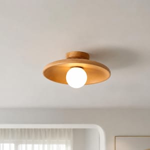 Peut inclure: Un plafonnier en bois avec un abat-jour en forme de chapeau. L'abat-jour présente une finition en bois clair et entoure une ampoule sphérique blanche. La lumière est fixée au plafond blanc, offrant un design minimaliste. Le diamètre est d'environ 30 cm.