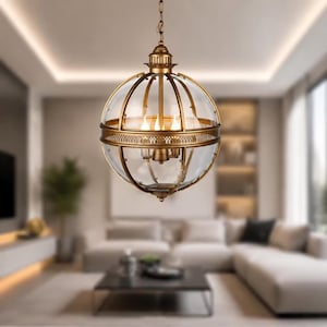 May include: A spherical chandelier in an antique style, featuring a clear glass globe and a bronze-coloured metal frame. The fixture has three lights and is suspended from a chain. The design is reminiscent of vintage lighting.