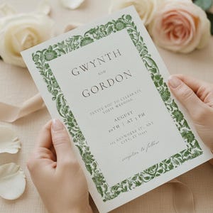 May include: A wedding invitation held by hands, featuring the names "Gwynth and Gordon" in a serif font. The invitation has a green floral border and includes the date, time, and location of the wedding. Soft pink and white roses are in the background.