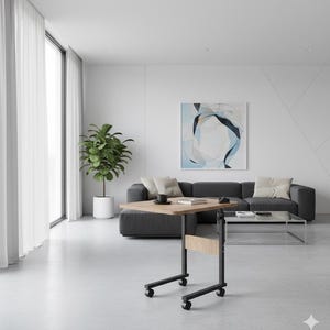 May include: A mobile, height-adjustable table with a light wood top and black metal frame. The table is on wheels and is positioned in front of a grey sofa. A coffee cup and book rest on the table. The room has a modern design with a large window and abstract art.