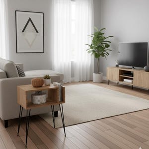 May include: A modern living room with light wood flooring, a beige sofa, and a wooden side table with black hairpin legs. A large rug and a potted plant add warmth. A framed abstract art piece hangs on the wall.