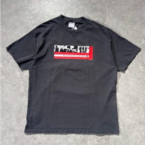 May include: Dark gray t-shirt featuring a rectangular graphic with a red stripe and black and white silhouettes. The text "UP ELEVATION TOUR 2001" is printed on the graphic. The shirt has a crew neck and short sleeves.