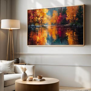 May include: A framed landscape painting depicts a vibrant autumn scene. The artwork showcases a river reflecting the colorful trees in shades of red, orange, and yellow. The painting is displayed above a white sofa and round wooden coffee table.