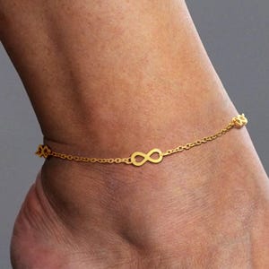 Peut inclure: Un bracelet de cheville doré orné de symboles infinis. La chaîne délicate est ornée de plusieurs symboles infinis, créant un accessoire élégant et symbolique. Le bracelet de cheville est porté sur la cheville.