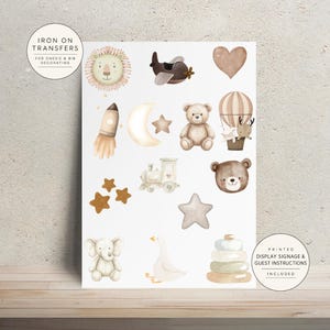 May include: A sheet of iron-on transfers featuring watercolor illustrations of a lion, airplane, heart, rocket, moon, stars, teddy bear, hot air balloon, train, elephant, goose, and stacking rings. Text reads IRON ON TRANSFERS FOR ONESIE & BIB DECORATING.
