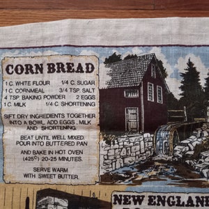May include: A vintage kitchen tea towel with a recipe for cornbread printed on it. The towel features a rustic illustration of a New England farmhouse with a water wheel. The recipe includes ingredients like white flour, cornmeal, sugar, salt, baking powder, eggs, milk, and shortening. The text reads "CORN BREAD" and "NEW ENGLAND".
