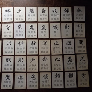 May include: A collection of small, rectangular cards with black Japanese characters printed on a white background. The cards are arranged on a dark surface, likely for a game or educational purpose.