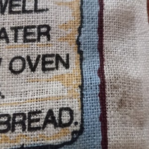 May include: A white linen kitchen towel with a blue and red border. The text "Use well water, slow oven, good friends, and fresh bread." is printed in black on the towel.