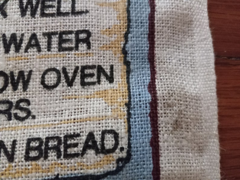 May include: A white linen kitchen towel with a blue and red border. The text "Use well water, slow oven, good friends, and fresh bread." is printed in black on the towel.