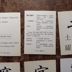 May include: Several small white cards with Japanese text and English translations are arranged on a textured brown surface. The cards feature words like "dragon" and "abbreviation", with corresponding definitions.