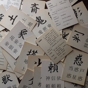 May include: A collection of vintage flashcards with Japanese characters and English definitions. The cards are arranged in a scattered pattern, with the black ink characters standing out against the aged paper.