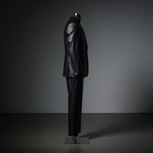 May include: A black leather suit displayed on a mannequin. The suit includes a blazer with buttoned cuffs and matching trousers. The outfit is presented against a dark gray backdrop, highlighting the sleek design and texture of the leather.