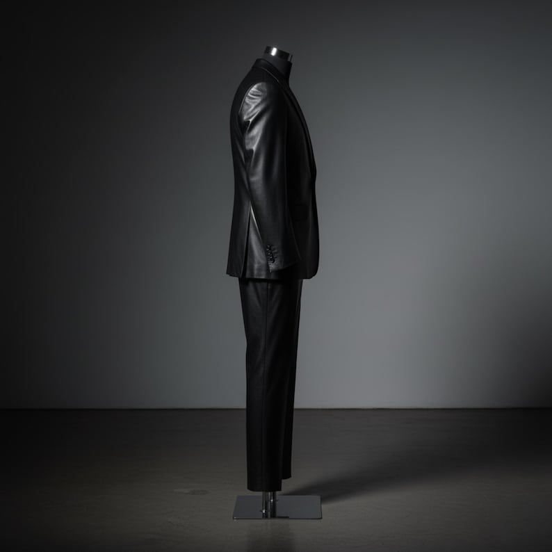 May include: A black leather suit displayed on a mannequin. The suit includes a blazer with buttoned cuffs and matching trousers. The outfit is presented against a dark gray backdrop, highlighting the sleek design and texture of the leather.